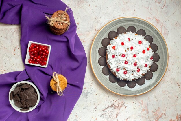 Top view cake on plate cookies tied with rope bowls with berries and chocolate on purple shawl