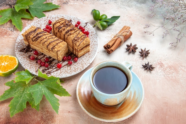 Top view cake slices with cup of tea and red berries on light desk biscuit sweet cake