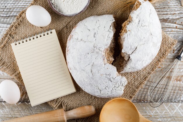 Top view cake with notepad, eggs, rolling pin on sack cloth and wooden surface. horizontal