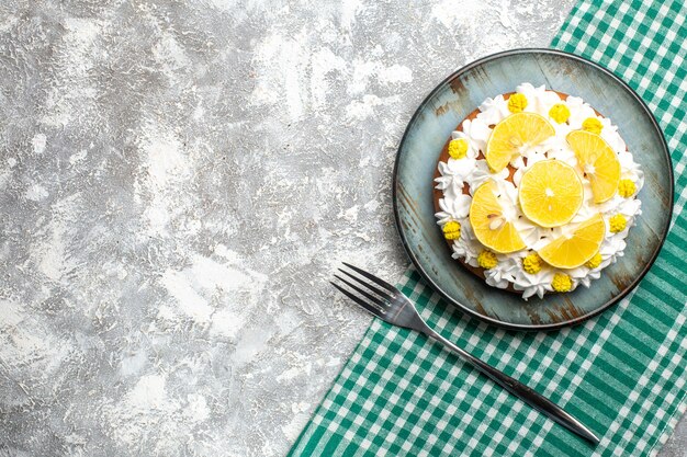 Top view cake with pastry cream and lemon on round plate fork on green white checkered tablecloth