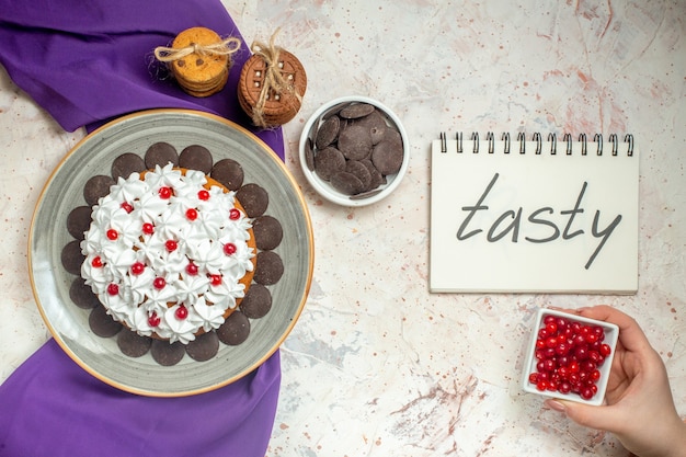 Free Photo top view cake with pastry cream on oval plate purple shawl cookies tied with rope chocolate bowl tasty written on notebook