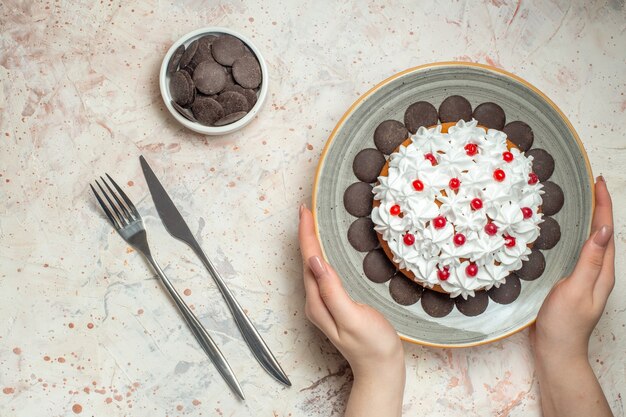 Top view cake with pastry cream on plate in female hand chocolate in bowl fork and dinner knife