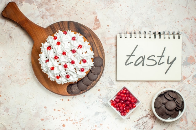 Free photo top view cake with white pastry cream on wooden cutting board tasty written on notebook