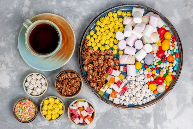 Free photo top view candy composition different colored candies with marshmallow and cup of tea on the light white desk sugar candy bonbon sweet confiture