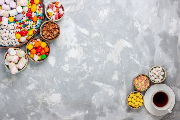 Top view candy composition different colored candies with marshmallow and tea on the white desk sugar candy bonbon sweet confitures