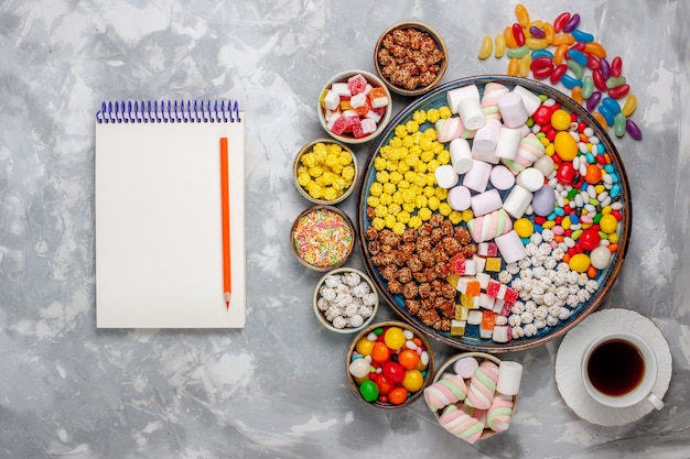 Free photo top view candy composition different colored candies with notepad marshmallow and tea on white desk sugar candy bonbon sweet confiture