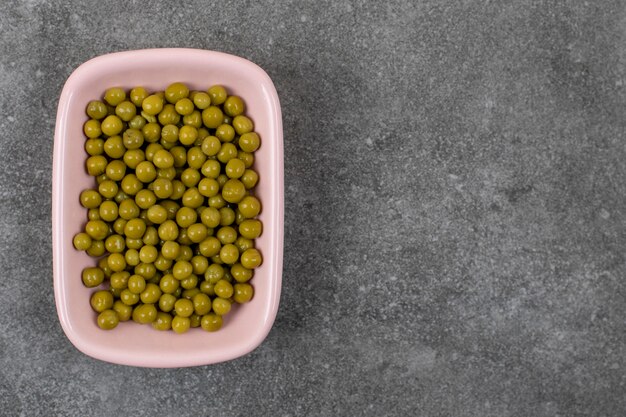 Top view of canned Green peas in pink bowl over grey table.