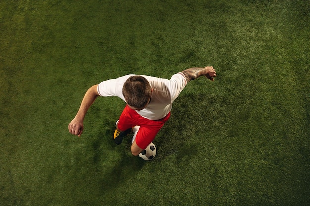 Free photo top view of caucasian football or soccer player on green background of grass. young male sportive model training, practicing. kicking ball, attacking, catching. concept of sport, competition, winning.