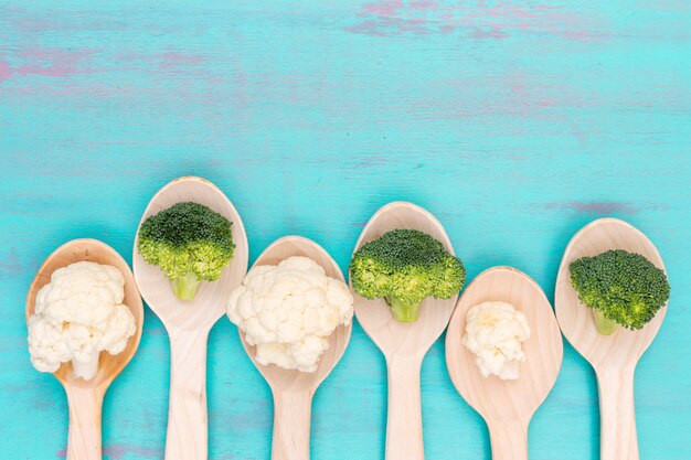 Top view cauliflower and broccoli in wooden spoons with copy space on blue surface