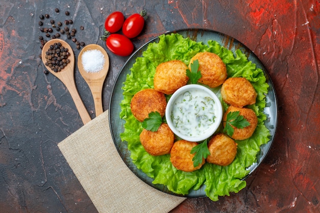 Free Photo top view cheese balls on plate with lettuce and sauce cherry tomatoes wooden spoons black peppers on dark surface