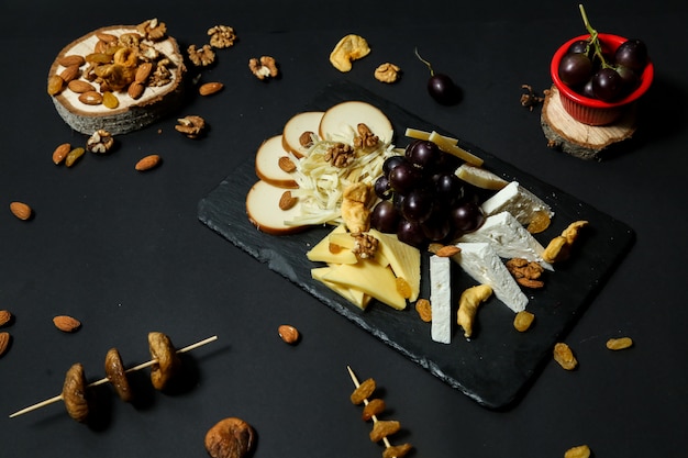 Free photo top view cheese plate with grapes and nuts on a stand with dried fruits on a black table