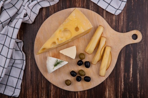 Top view cheese varieties with olives on a stand with a checkered towel on a wooden background