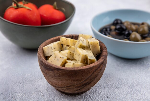 Top view of cheese on a wooden bowl with fresh tomatoes and olives on a white background