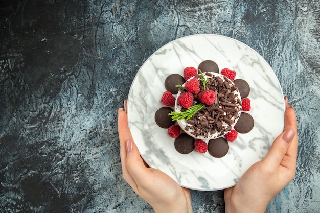 Top view cheesecake with chocolate on oval plate in woman hands on grey surface free place