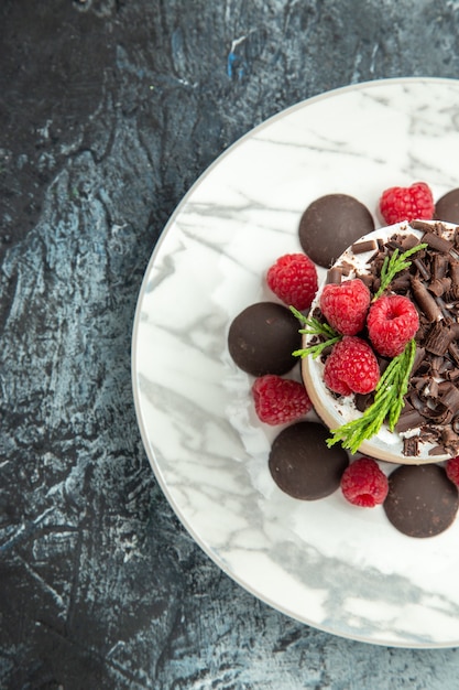 Top view cheesecake with chocolate and raspberries on white oval plate on grey surface