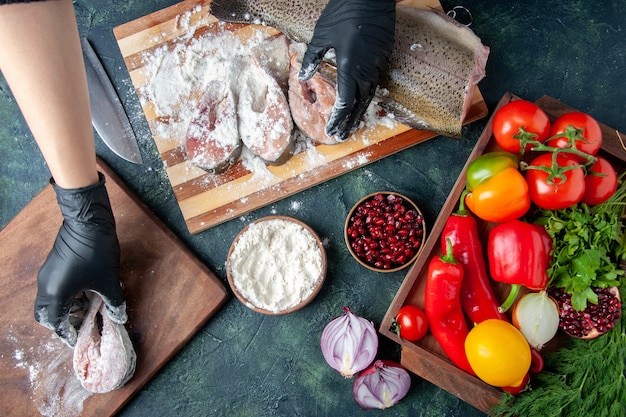 Top view chef covering fish slices with flour fresh vegetables on wood board flour bowl on kitchen table