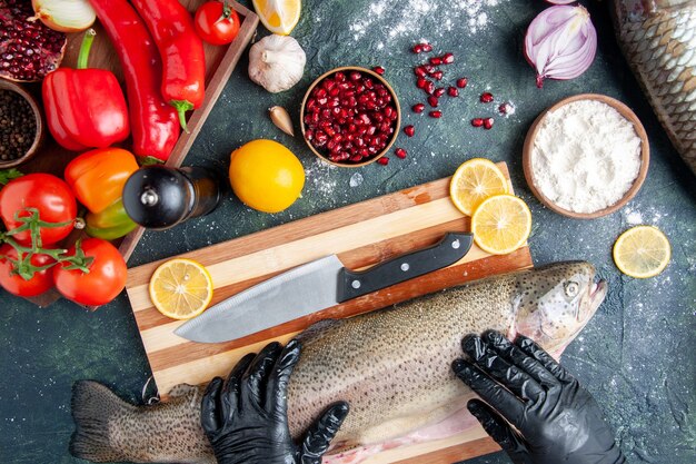 Top view chef with black gloves holding raw fish on wood board pepper grinder flour bowl pomegranate seeds in bowl on kitchen table