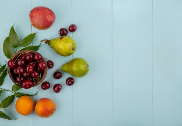 Top view of cherries in bowl and pattern of pears apricots peach cherries with leaves on blue background with copy space