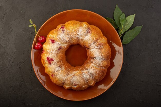 A top view cherry cake round formed inside brown plate on the dark desk cake biscuit sugar sweet