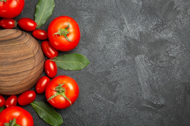 Free photo top view cherry and red tomatoes bay leaves around a wooden plate on the left of dark ground with copy spase