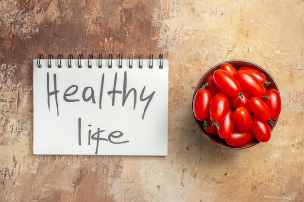 Free Photo top view cherry tomatoes in wooden bowl healthy life written on a notepad on amber background