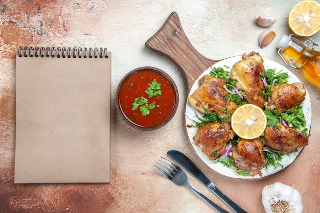 Top view of chicken chicken with lemon herbs on the board oil fork knife cream notebook