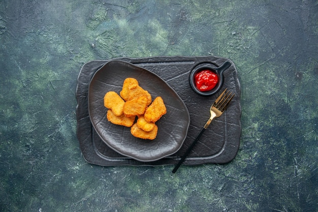 Free Photo top view of chicken nuggets on a black plate and fork ketchup on dark color tray on dark surface