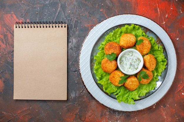 Free Photo top view chicken nuggets lettuce and sauce on plate notebook on dark table