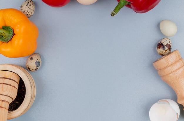 Top view of chicken and quail eggs with bell pepper with wooden mortar and pestle with salt shaker on a white background with copy space