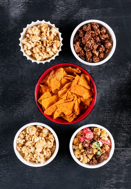 Top view of chips and popcorn in bowls on black  vertical