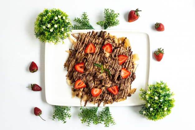 A top view choco strawberry dessert yummy sweet along with whole strawberries and plants spread all over the white background fruit cake