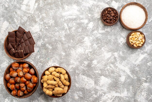 Top view of chocolate bars with hazelnuts and peanuts on white surface