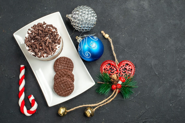 Free photo top view chocolate cake and biscuits on white rectangular plate xmas tree toys on dark isolated background