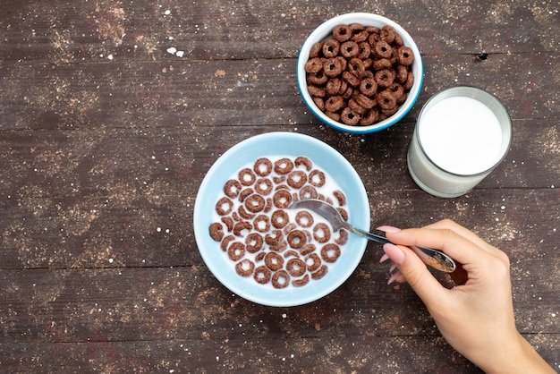 Top view chocolate cereals with milk inside blue plate and along with spoon on brown