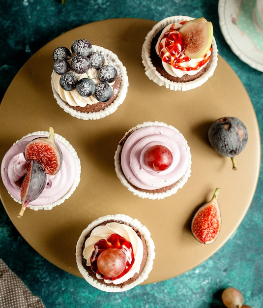 Free photo top view of chocolate cupcakes decorated with vanilla cream figs grapes and blueberries