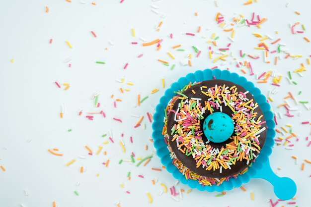 A top view chocolate donut with little colorful candies on white desk, candy color sweets