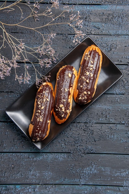 Top view chocolate eclairs on dark rectangle plate on the dark wooden table with free space