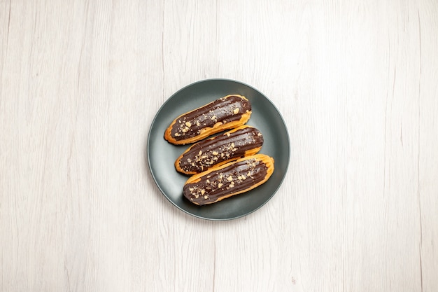 Free photo top view chocolate eclairs on the grey plate in the center of the white wooden ground