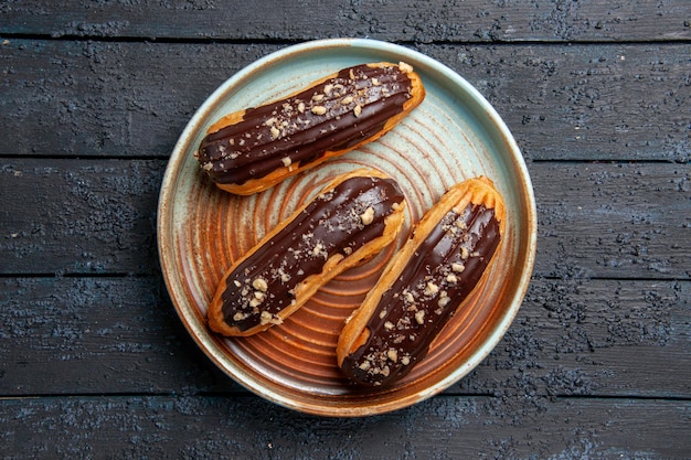 Free photo top view chocolate eclairs on oval plate on the dark wooden table with free space