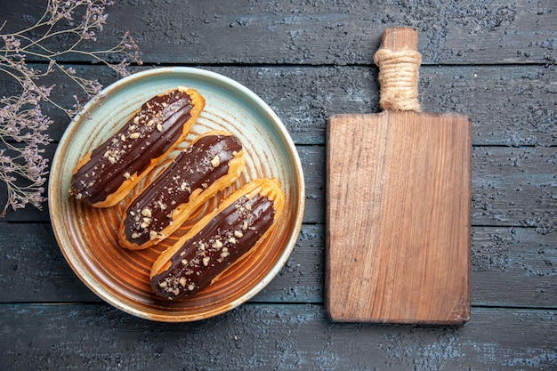 Free photo top view chocolate eclairs on oval plate dried flower branch and chopping board on the dark wooden table