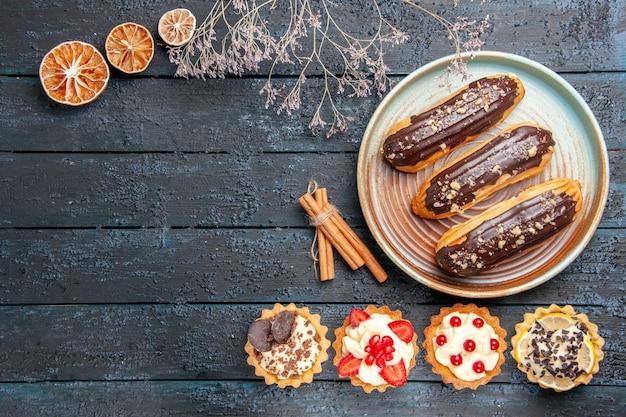 Free photo top view chocolate eclairs on oval plate tarts cinnamon dried oranges on the dark wooden table with copy space