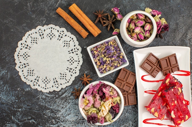 Free photo top view of chocolate on white plate and white lace with bowls of dry flowers on grey ground