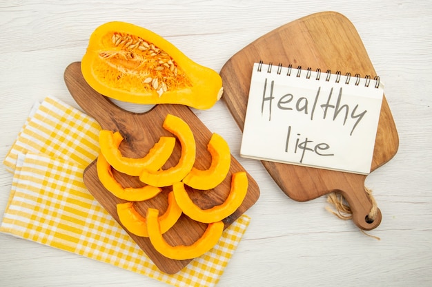 Top view chopped butternut squash on chopping board on yellow white checkered kitchen towel healthy life written on notepad on cutting board on grey table