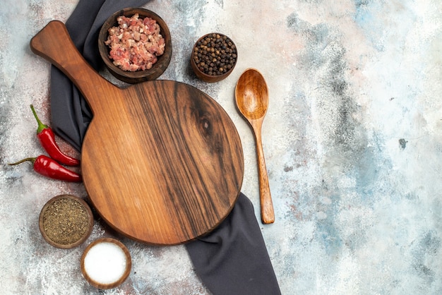 Top view chopping board black tablecloth bowls with meat different spices wooden spoon on nude surface copy space