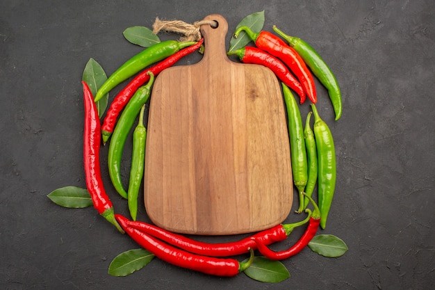 Top view a chopping board in the circle of red and green hot peppers and pay leaves on black background