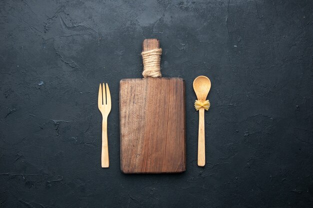 Top view chopping board wooden spoon and fork on dark surface copy space