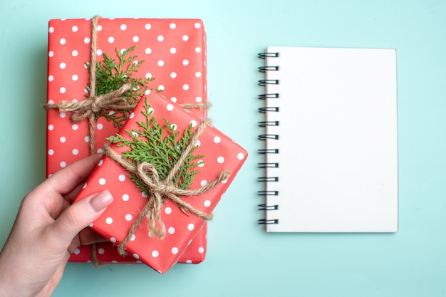 Top view of Christmas background with hand holding red gift boxes and notebook on pastel green background