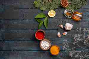 Free photo top view christmas dish bottle of oil bowls of spices lemon garlic spruce branches with cones on the dark table