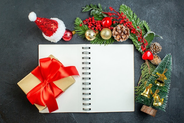 Top view of christmas mood with fir branches santa claus hat xsmas tree gift box on notebook on dark background