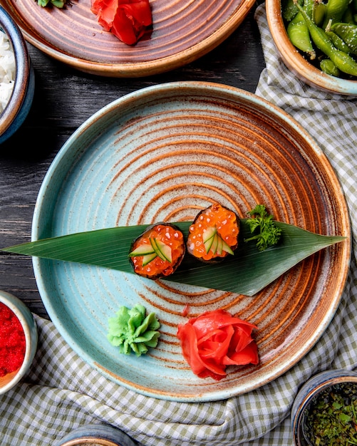 Free photo top view of classic japanese sushi with red caviar on bamboo leaf served with ginger and wasabi sauce on a plate